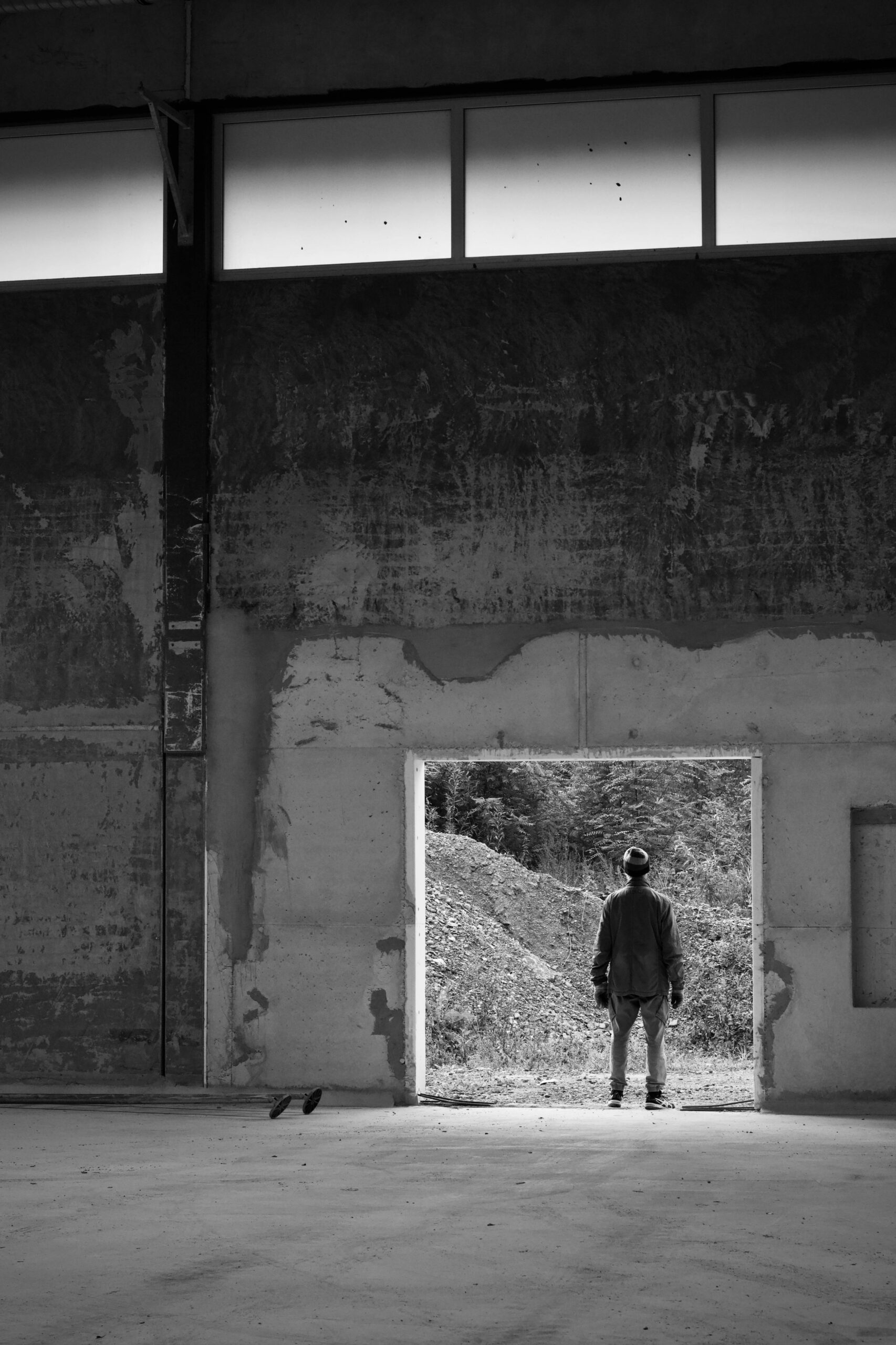 A lone person stands in a doorway of an abandoned industrial building, gazing outside.